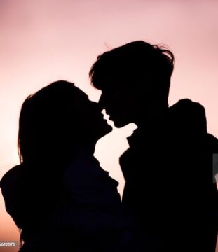 Silhouette Of Teenage Couple Kissing At Sunset.