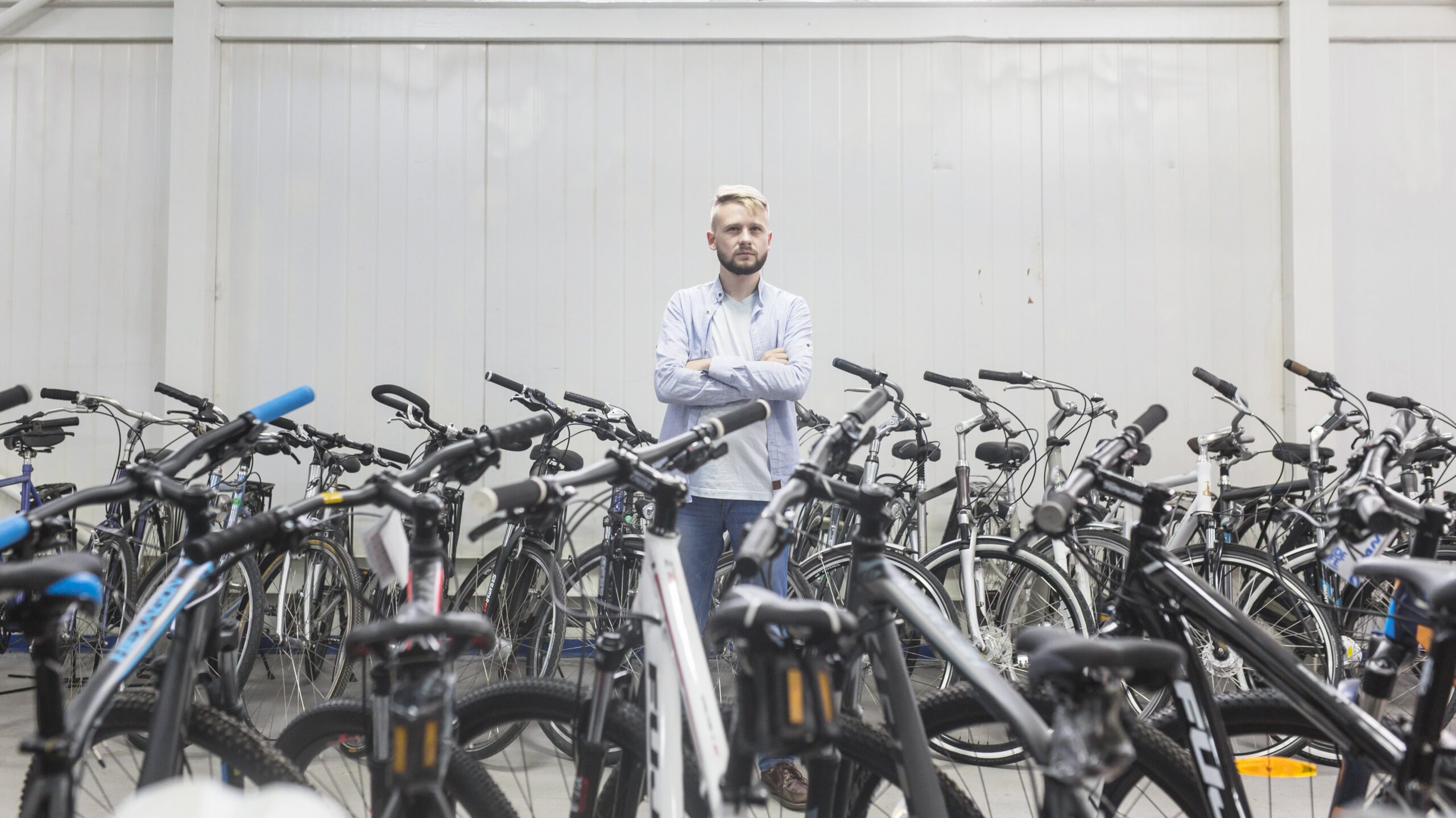 Various Bicycles Surrounding Male Mechanic Standing Workshop (1)